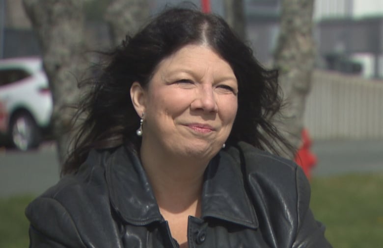 A woman with black hair blowing in the wind wearing a black jacket.